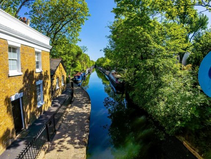 Calm waters of regent's canal reflecting surrounding trees and buildings under a bright sun,