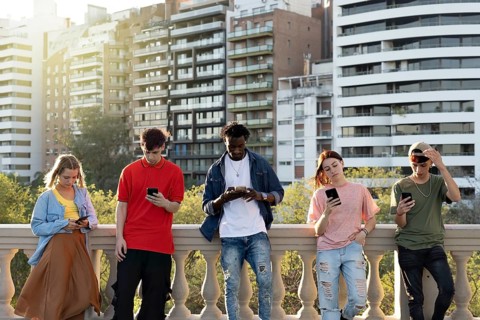 Young people looking down at cellular phone. Teenagers leaning on a wall and texting with their
