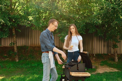 A middle-aged man cooks a beef steak on the grill for his daughter, who came to visit him at a