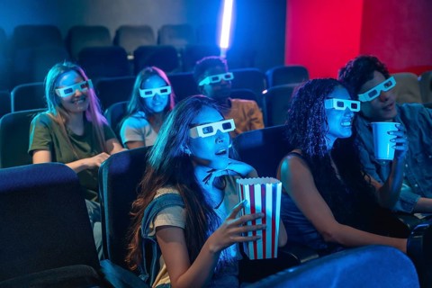 Group of excited young friends wearing 3d glasses, watching a movie at the cinema, eating popcorn