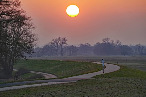 A winding path leads through a landscape under a glowing sunset, Elbe dyke, Damnatz, Elbe cycle