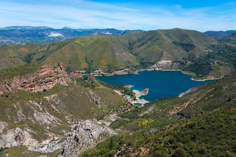 Panoramic view of a blue lake surrounded by green mountains and rocks under a clear sky, reservoir,