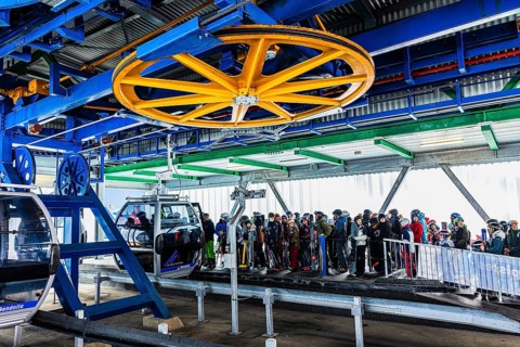 Skiers queue at the valley station for the ascent with the cable car to the Bendolla ski area,