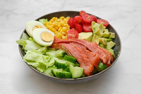 A poke bowl with iceberg lettuce, smoked salmon, boiled eggs, sweet corn, cherry tomatoes, and
