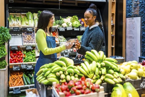 Friendly saleswoman handing a packaged product to a customer in a supermarket with shelves full of