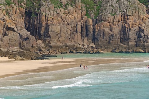 Sandstrand mit hohen Klippen und ruhigem türkisfarbenem Meer, wenige Menschen, Porthcurno, St