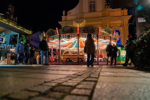 An illuminated carousel with people surrounded by a nocturnal city atmosphere, Christmas market