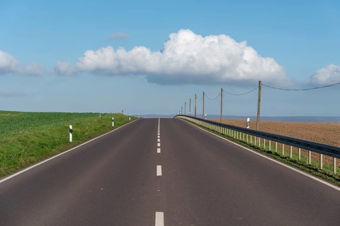 Empty main road, old wooden electricity pylons, white cloud in the blue sky, Halberstadt,