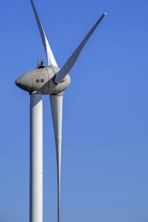 Wind turbine close-up showing tower, nacelle and huge rotor blades against blue sky