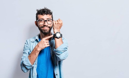 Person pointing at his watch looking at the camera. Friendly man pointing his wrist watch on