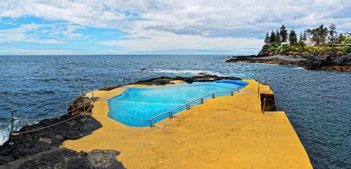 Natural swimming pool on rocks overlooking the ocean and cliffs under a cloudy sky, Caloura,