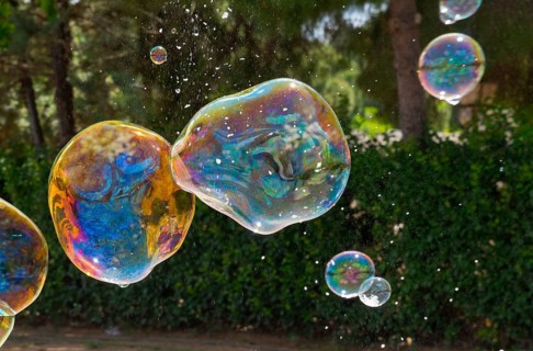 Colourful soap bubbles float in front of a green hedge in nature, Spain