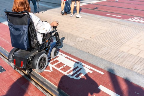 Woman navigating an electric wheelchair across designated tram tracks in a city environment,