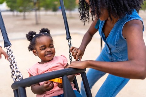 African mother and baby girl having fun swinging in a public park
