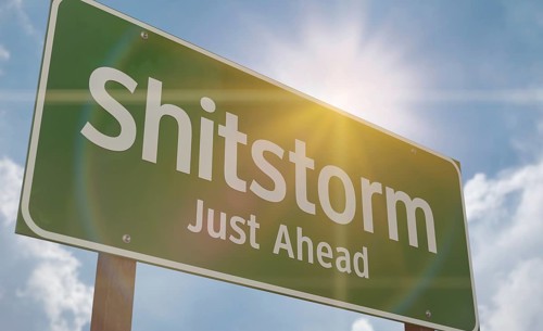 Shitstorm just ahead green road sign against a blue sky and clouds