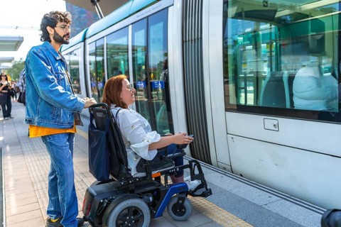 Young man assisting mid adult woman in a wheelchair as they board a modern tram at a bustling city