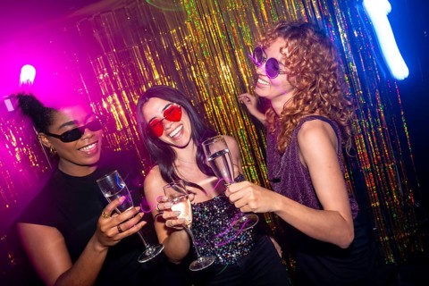 Multi ethnic female friends are having fun together, toasting with champagne flutes and laughing at