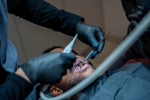 Dentist wearing black gloves examining patient's teeth with dental instruments during checkup in