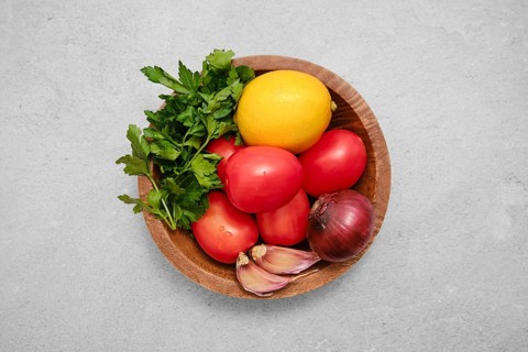 A wooden bowl holds ripe tomatoes, fresh lemon, and vibrant herbs, showcasing the beauty of fresh