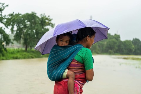 A tribal woman with her child stands with umbrella during a heavy rain in Golapara, India on 31 May