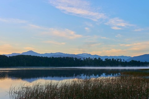 A still lake with a misty water surface and mountains in the background in the early morning, Lake