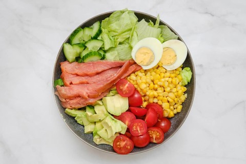 A vibrant salad bowl features layers of crisp lettuce, smoked salmon slices, boiled eggs, sweet