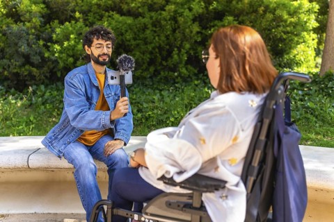 Content creator interviewing a businesswoman in a wheelchair using a smartphone and microphone in a