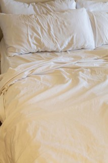 Close-up of rippled and creased white cotton bed sheets and pillows on unmade king size bed, La
