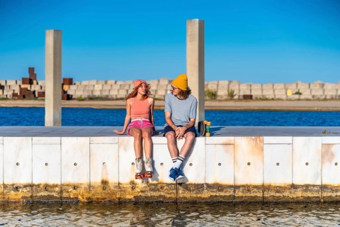 Young skaters enjoying a sunny day at the pier, talking and relaxing by the water with roller