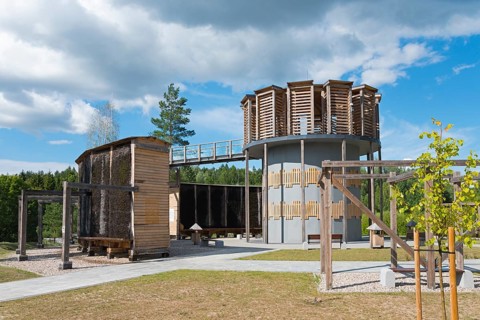 Modern wooden construction with round tower and evaporation walls, surrounded by greenery and clear