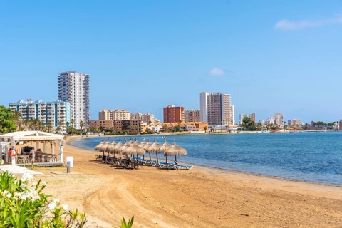 Tranquil beach scene with straw umbrellas and lounge chairs, overlooking the cityscape of la manga