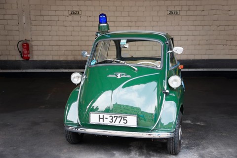 Green vintage tricycle with blue light in garage in front of brick wall, BMW Isetta 300, scooter