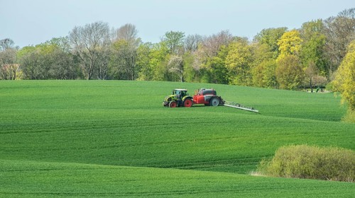 Spring farming, spreading fertilizer on a field with crops with a tractor at a forest in Ystad