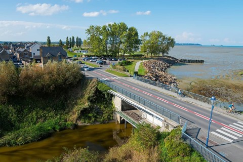 Coastal landscape with a bridge over a river, lined with houses and trees, overlooking the sea,