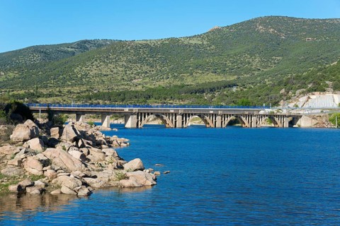 A picturesque landscape with a bridge over a river, surrounded by green mountains and blue sky,