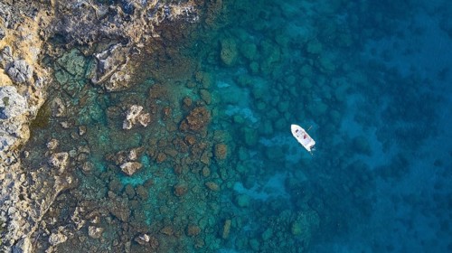 Drone shot, boat in clear blue water next to rocks and corals, Anthony Quinn Bay, Vagies Bay,