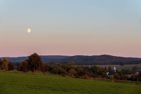 Evening mood with moon, the hills of the Upper Lusatian Highlands and the village church of