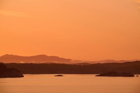 Atmospheric landscape scene at sunrise with pastel-coloured sky, calm sea and silhouetted islands