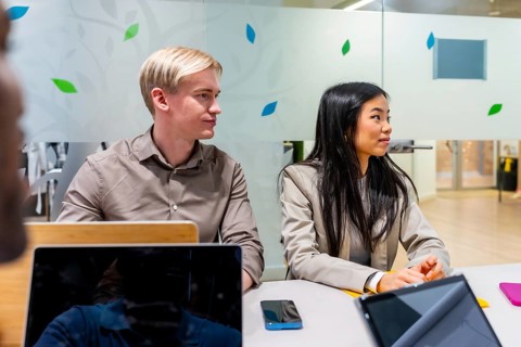 Two business professionals engaged in listening to a speaker during a meeting held in a modern