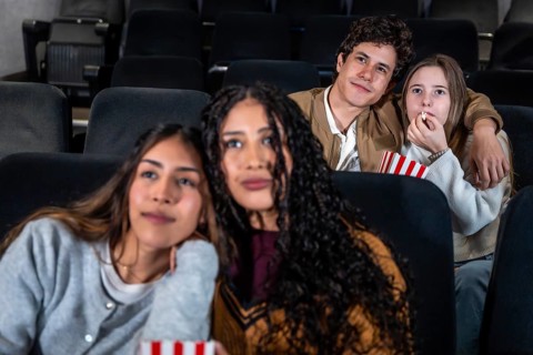 Group of friends enjoying a film at the movie theater, sharing popcorn and having fun together
