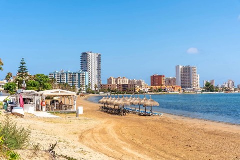 Straw umbrellas and beach chairs sit on the sandy shore of la manga, with resort hotels and