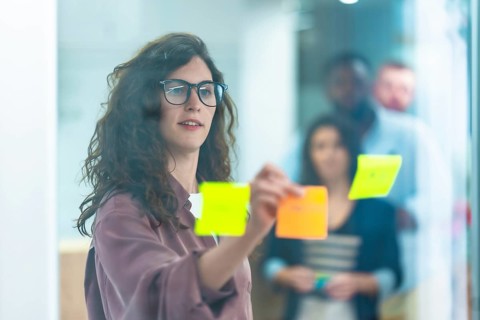 Focused businesswoman attaching colorful sticky notes on a glass wall during a brainstorming
