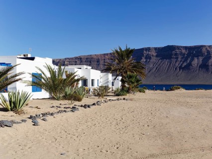 White holiday homes, palm trees on a sandy beach, Risco de Famara cliffs, Caleta del Sebo, La