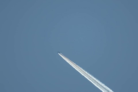 Boeing 777 aircraft flying across a blue sky leaving a contrail or vapor trail in the atmosphere