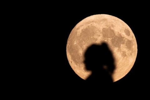 The silhouette of a woman stands out against the rising full moon. A supermoon will shine from the