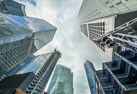 An upward view capturing the dynamic architecture of towering skyscrapers under a cloudy sky in a
