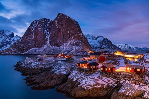 Fishermen's Village in front of snowy mountain range at the coastline in winter, Lofoten, Norway
