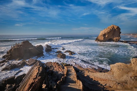Penedo do Guincho stands majestically at Praia da Santa Cruz as ocean waves crash against it,
