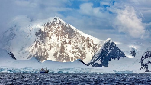 A ship sails along snow-covered mountains, surrounded by ice and clouds, in a cold and dramatic