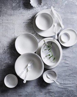Top view of an elegant arrangement of white ceramic dishes and utensils on a textured grey